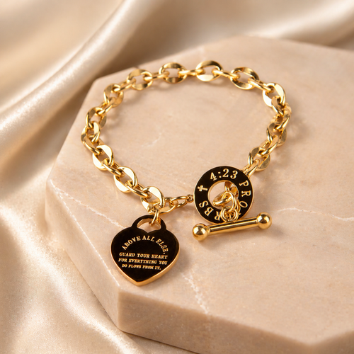 Gold Guard Your Heart Bracelet with heart-shaped tag and round tag on a beige stone surface